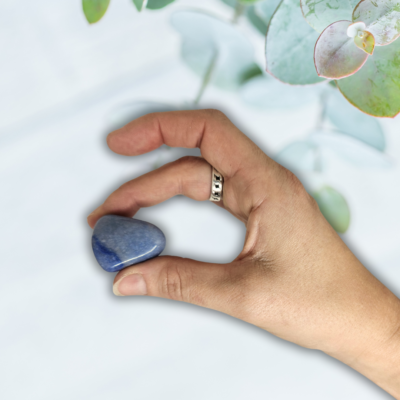 Een hand met die met twee vingers een blauwkwarts trommelsteen vast houdt.