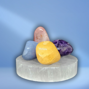 Een roze agaat abrikoos, paarse amethist, blauw kwarts en oranje calciet. Deze vier edelstenen liggen op een ronde witte seleniet oplaadsteen.